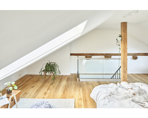 Chambre lumineuse dans les combles avec fenêtre de toit, poutres en bois et plancher en bois