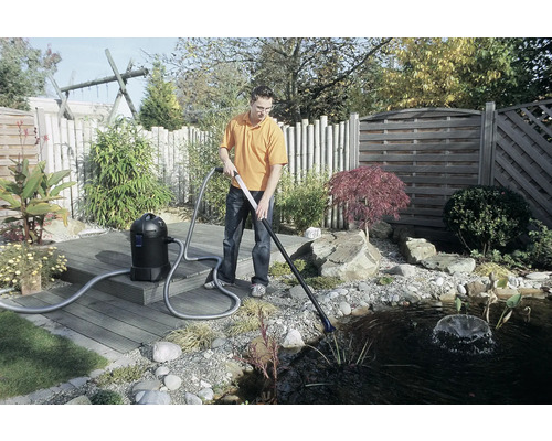 Un homme nettoie un bassin avec un aspirateur de vase de bassin dans le jardin.