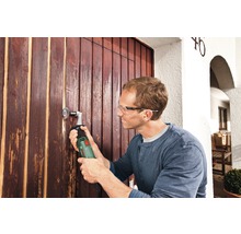 Un homme ponce une porte en bois avec un outil électrique.