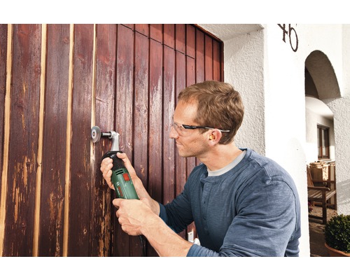 Un homme ponce une porte en bois avec un outil électrique.