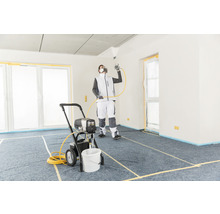 Un homme utilise un pulvérisateur de peinture dans une pièce recouverte pour des travaux de peinture.