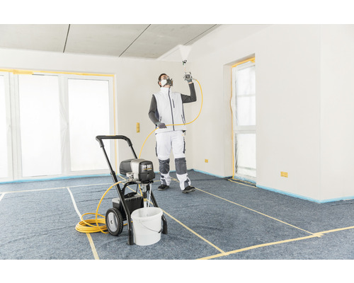 Un homme utilise un pulvérisateur de peinture dans une pièce recouverte pour des travaux de peinture.