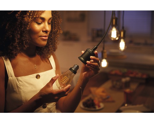 Frau wechselt eine klare Filament-Glühbirne in eine schwarze Lampenfassung.