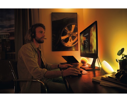 Szene eines Mannes, der mit Headset vor einem Computer sitzt, beleuchtet von zwei Tischleuchten