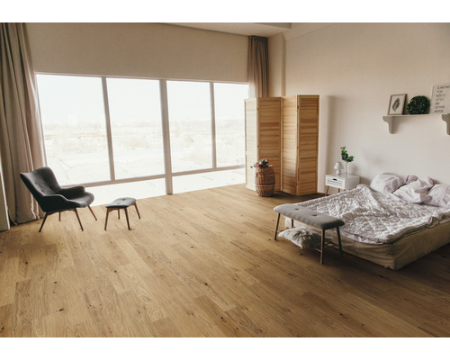 Heller Schlafzimmerraum mit Holzboden, Sessel, Bett und großem Fenster.