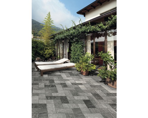 Terrasse avec carrelage aspect pierre, chaises longues et plantations devant une maison