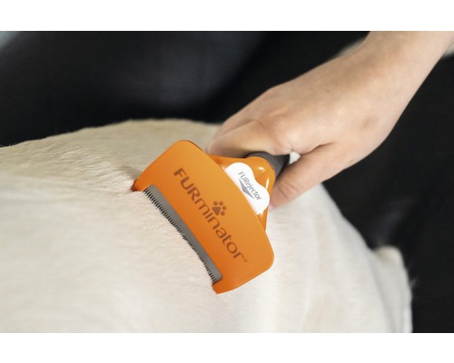 Eine Hand benutzt eine Fellbürste von Furminator auf dem Fell eines Tieres.