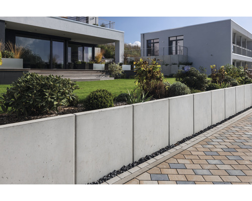 Garten mit Betonstützmauer und Pflasterweg vor modernen Häusern