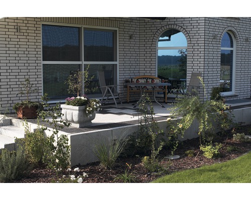 Terrasse avec mobilier de jardin et jardinières fleuries devant une maison avec une façade en briques.