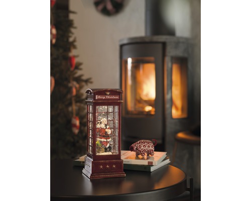 Dekorative Schneekugel in Form einer Telefonzelle mit Weihnachtsmannmotiv und Kamin im Hintergrund.