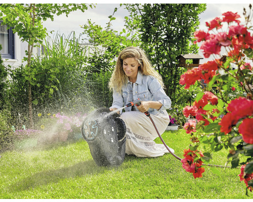 Eine Frau reinigt einen Rasenmähroboter mit einem Gartenschlauch in einem Garten.