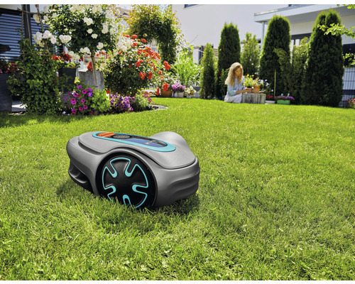 Robot tondeuse sur pelouse dans jardin avec fleurs et une femme