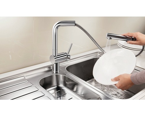 Évier en acier inoxydable avec robinet chromé et douchette en train de laver une assiette