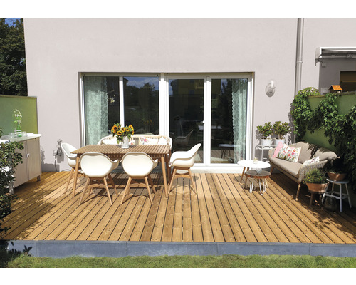 Terrasse avec plancher en bois, table de jardin et chaises devant une maison