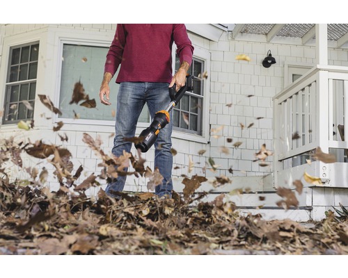 Un homme utilise un aspirateur de feuilles devant une maison.