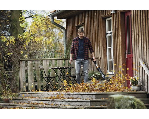 Un homme utilise un souffleur de feuilles sur une terrasse en bois d''une maison