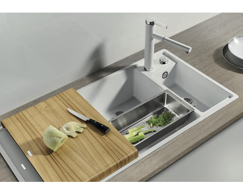 Évier avec planche à découper, égouttoir et robinetterie dans un environnement de cuisine lumineux.