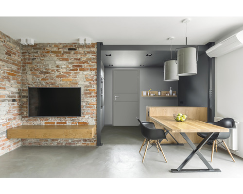 Salon avec mur de briques, télévision, table en bois et chaises.