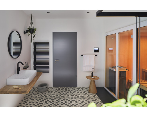 Helles Badezimmer mit Waschbecken, Spiegel, Heizkörper, Tür und Sauna.