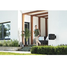 Gartenschlauchbox an einer Hauswand mit einer Frau auf der Terrasse
