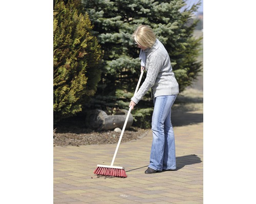 Une femme balaie une zone pavée dans le jardin avec un balai de voirie.