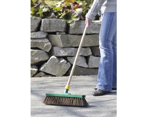 Une personne balaie une surface asphaltée à l''extérieur avec un balai.