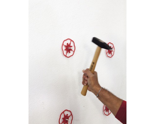 Ein Hammer schlägt Dämmstoffhalter in eine weiße Wand.