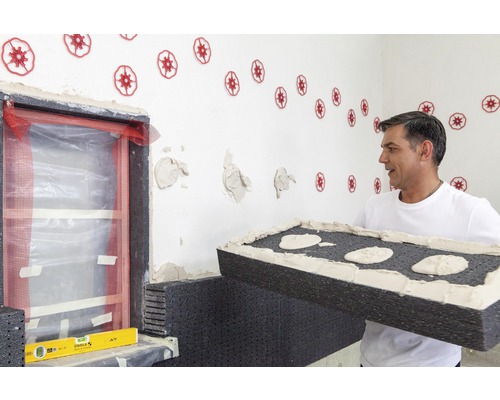 Mann bei der Anbringung von Fassadendämmplatten an einem Gebäude mit Fenster