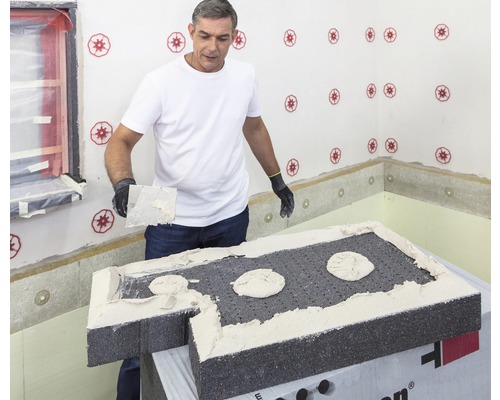 Mann verputzt Dämmplatte mit Spachtel in Innenraum