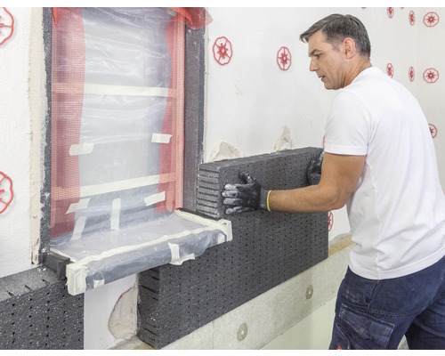 Ein Mann befestigt eine Dämmplatte an einer Hauswand.