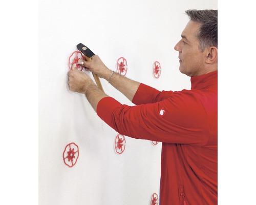 Mann befestigt Dämmstoffdübel mit einem Hammer an einer Wand