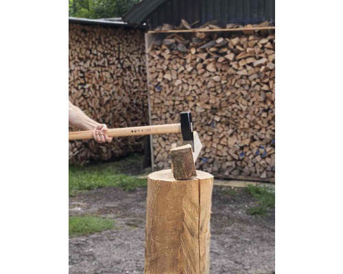 Holzhacken mit einer Axt auf einem Hackklotz vor einem Holzstapel