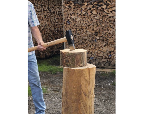 Mann spaltet Holz mit einer Spaltaxt auf einem Holzspaltblock vor einem Holzstapel