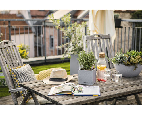 Scène de balcon avec table en bois, chaises, plantes, livre, chapeau et boissons pour une atmosphère de détente