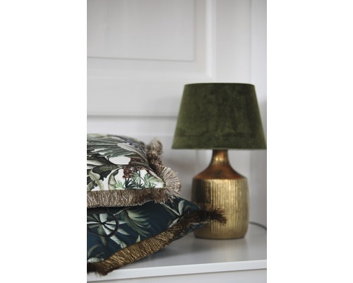 Coussins décoratifs à franges et lampe de table sur une étagère.