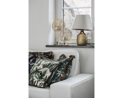 Salon décoratif avec canapé, coussins à motifs de jungle, lampe de table et bougeoirs chauffe-plat