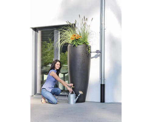 Une femme remplit un arrosoir à partir d''une haute colonne de tonneau à eau de pluie plantée.
