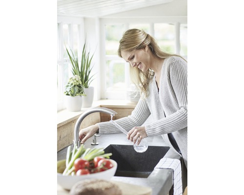 Femme lavant des légumes dans un évier de cuisine avec robinet.