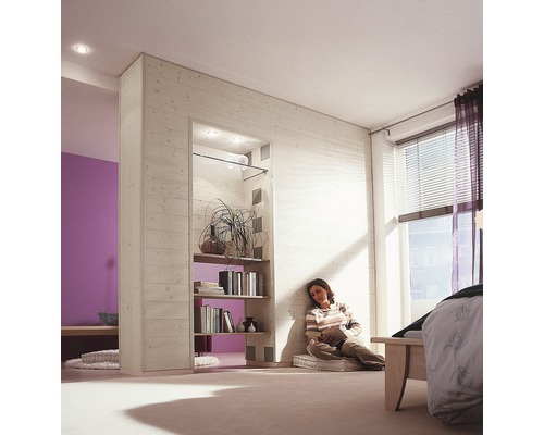 Une chambre avec une femme appuyée contre un mur en bois en train de lire un livre, avec une étagère remplie de livres et de décorations.