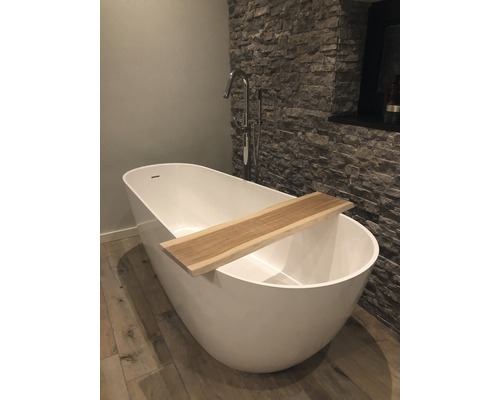 Baignoire îlot avec étagère en bois et robinet devant un mur en pierre