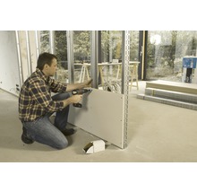 Un homme fixe une plaque de plâtre sur une structure métallique à l''aide d''une visseuse sans fil.