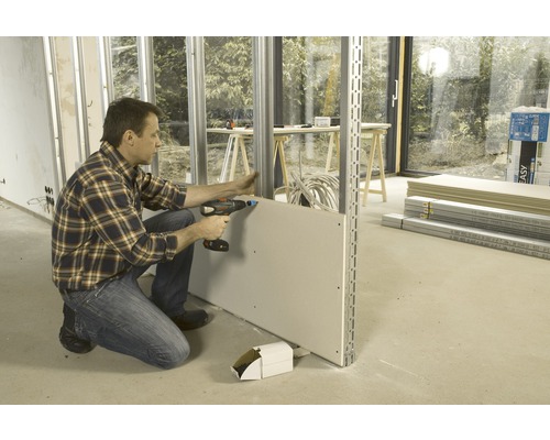 Un homme fixe une plaque de plâtre sur une structure métallique à l''aide de vis.