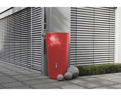 Récupérateur d''eau de pluie rouge avec robinet et trois boules de pierre dans le jardin
