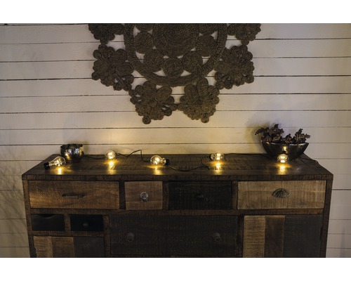 Commode avec tiroirs, décoration et guirlande lumineuse devant un mur en bois