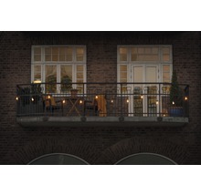 Balcon décoré avec guirlande lumineuse, chaises, table et plantes devant un bâtiment en briques.