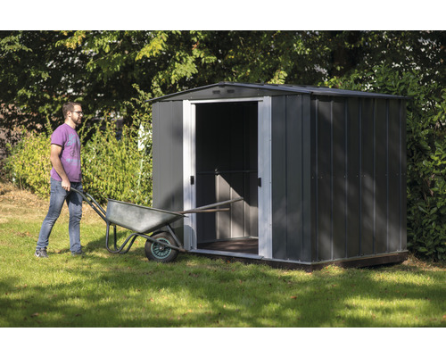 Gartenszene mit Metallgartenhaus und einer Person, die eine Schubkarre schiebt