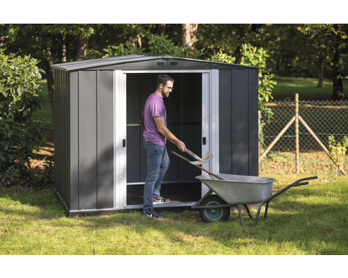 Gartenschuppen aus Metall mit Mann, Schubkarre und Gartengeräten im Garten