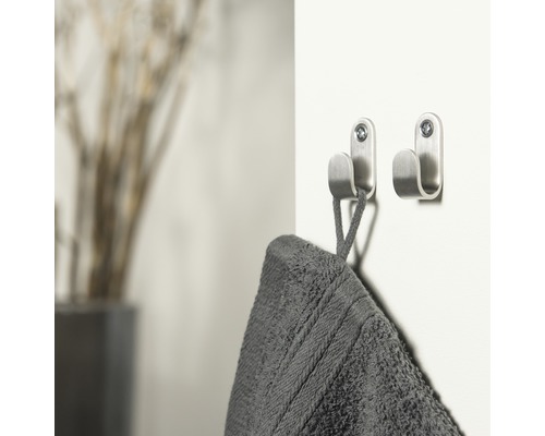 Zwei Handtuchhaken aus Metall sind an einer Wand befestigt, an einem hängt ein Handtuch.