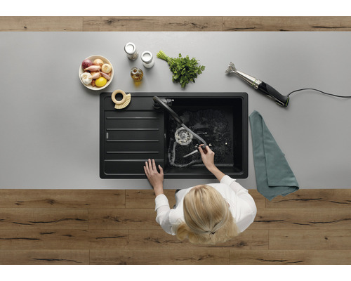 Vue de dessus d''une personne faisant la vaisselle dans un évier de cuisine noir, avec des aliments et des ustensiles de cuisine sur le plan de travail.