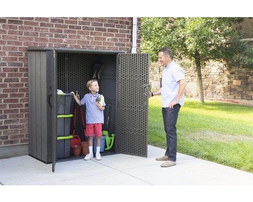 Gartenszene mit einem Geräteschuppen, in dem ein Kind steht, während ein Erwachsener die Tür öffnet
